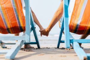 a couple holding hands while sitting in 2 beach chairs on the beach