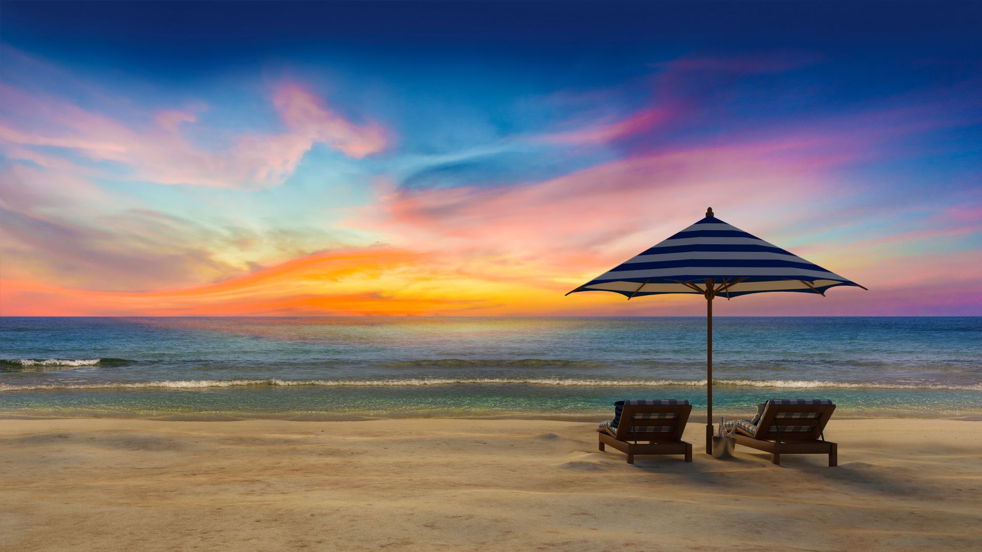 Two Adirondack chairs on the beach under a blue striped umbrella viewing a colorful pink, yellow and blue sunset